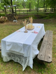 birthday Picnic table with white cloth, flowers, and candles on grass, next to a wooden bench.