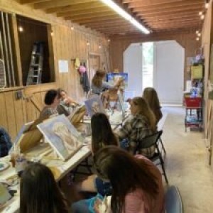 Group of people painting on canvases inside a wooden workshop.