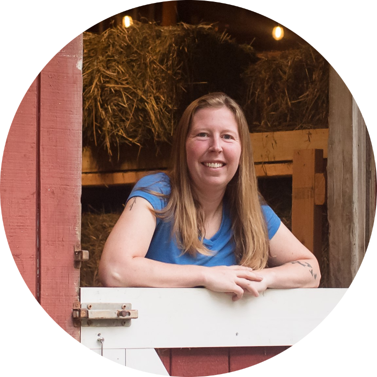 imgi_29_Rosero-71-modified Woman in blue shirt smiling, leaning on barn gate with hay in background.