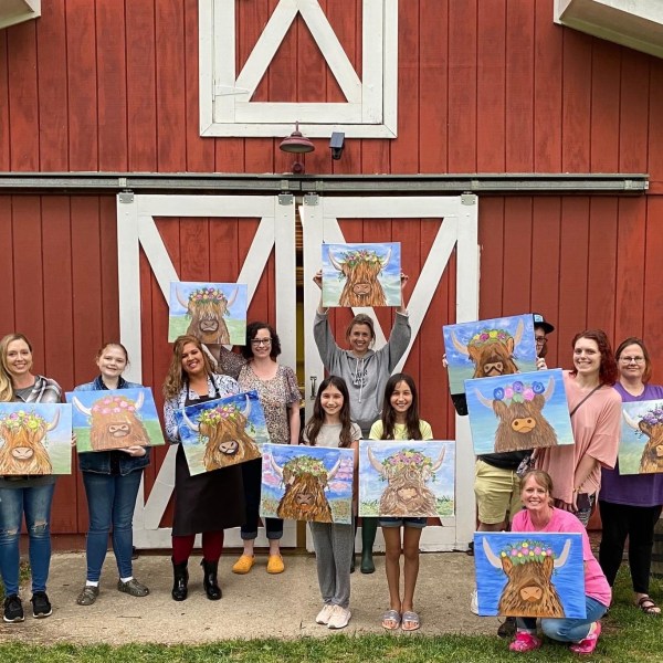 Group of people holding paintings of cows in front of a red barn.
