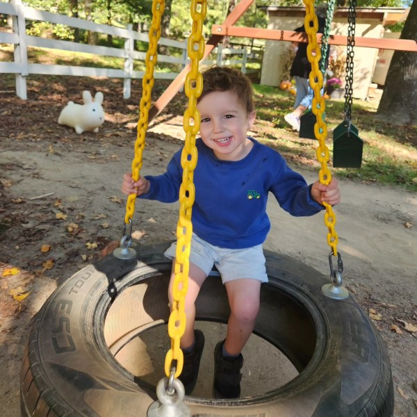 Young child smiling on a tire swing with yellow chains in a park.