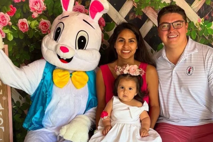 Family with a child poses next to a person in an Easter bunny costume, with roses in the background.